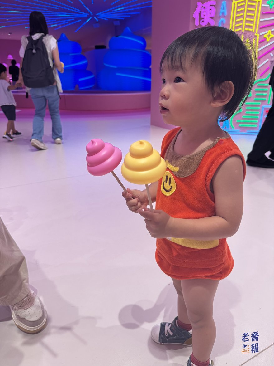 圈圈手上拿著粉紅色與黃色的彩色便便，開心看著展場
