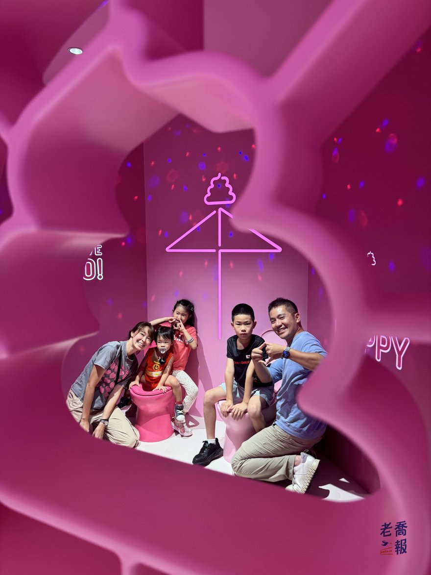 一家人蹲在粉紅色便便造型場景裡合照