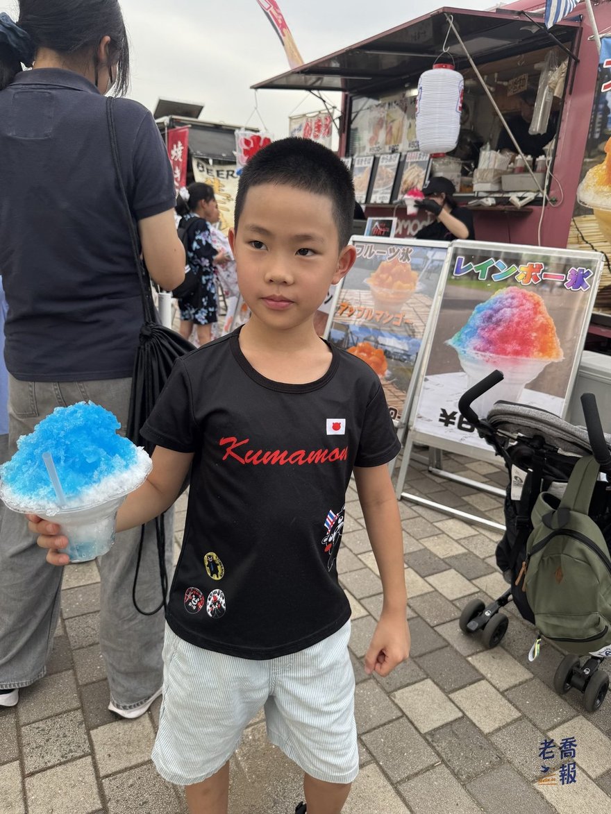嘻嘻拿著藍色刨冰站在攤位前，旁邊立牌寫著彩虹刨冰與水果刨冰