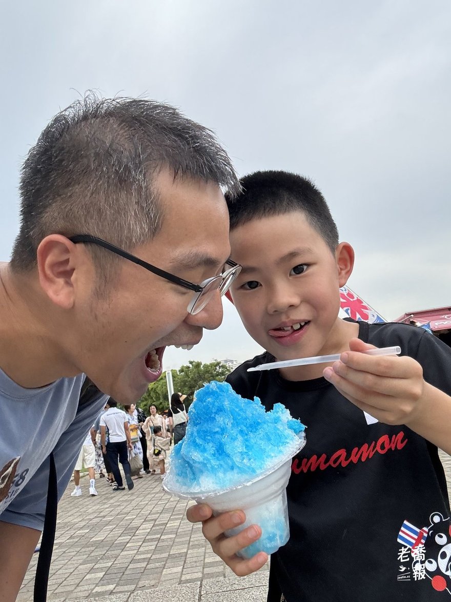 老喬張大嘴要偷吃嘻嘻手上的藍色刨冰，嘻嘻拿著吸管在旁邊笑