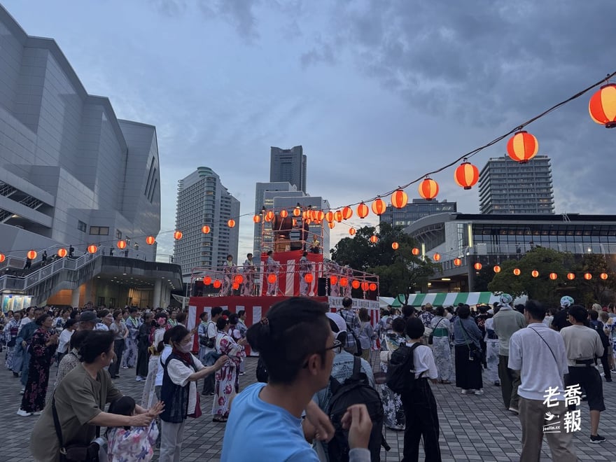 臨港公園廣場的大盆踊全景，紅色燈籠串橫過天空，中央是紅白布幔的櫓，後方是橫濱地標塔與港未來的高樓群