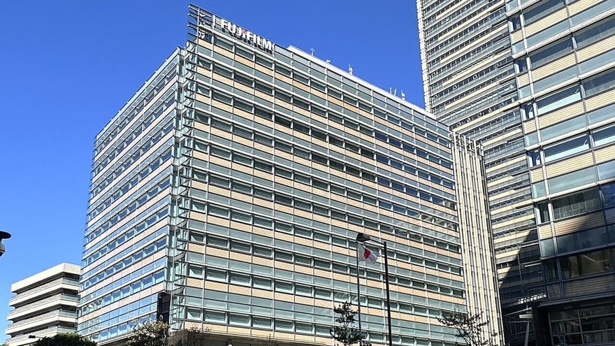 東京六本木東京中城旁的富士軟片總部大樓，十多層的玻璃帷幕建築頂端掛著 FUJIFILM 字樣，右側是更高的東京中城主塔，天空晴朗。