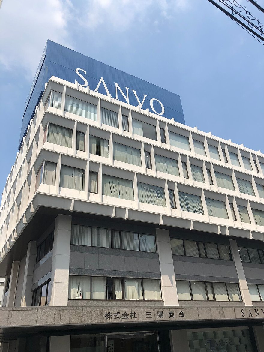 東京的三陽商會總部大樓：白色多層建築頂端是藍色招牌「SANYO」，一樓牆上寫著「株式会社 三陽商会」。