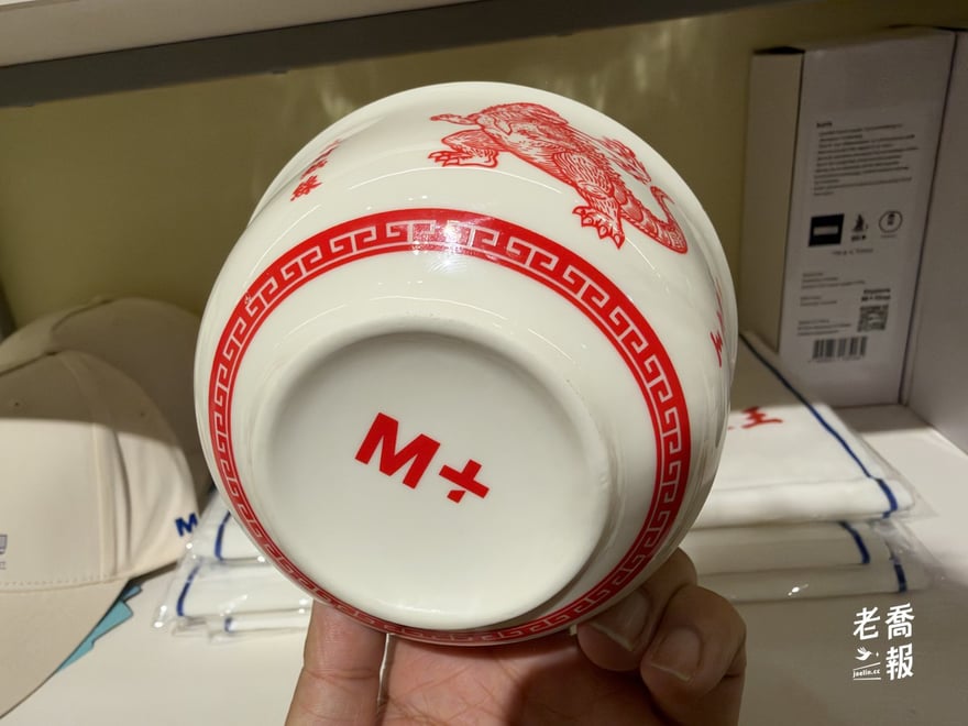 老喬把哥吉拉瓷碗翻過來拿在手上，碗底印著紅色的 M+ 標誌，碗緣一圈紅色回紋