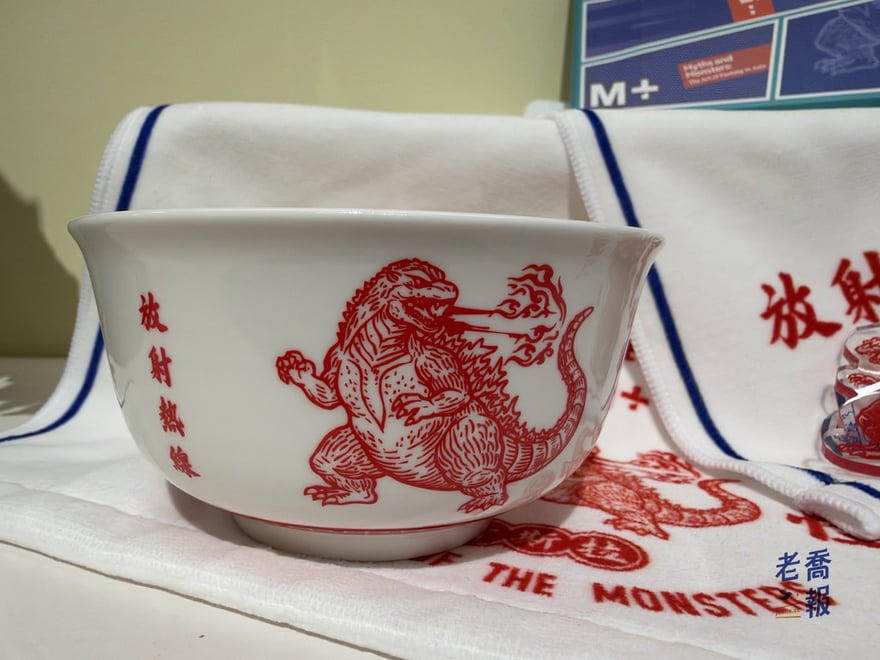 M+ 商店的哥吉拉瓷碗：白底紅線畫著噴火的哥吉拉，碗身直寫「放射熱線」，後面墊著同款紅字、藍邊的毛巾