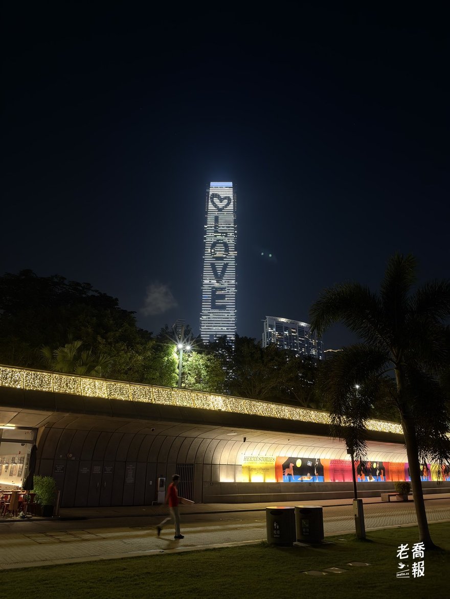 夜裡的環球貿易廣場（ICC）外牆燈光拼出一顆愛心和 LOVE 字樣，前面是西九公園的樹與亮燈的長廊