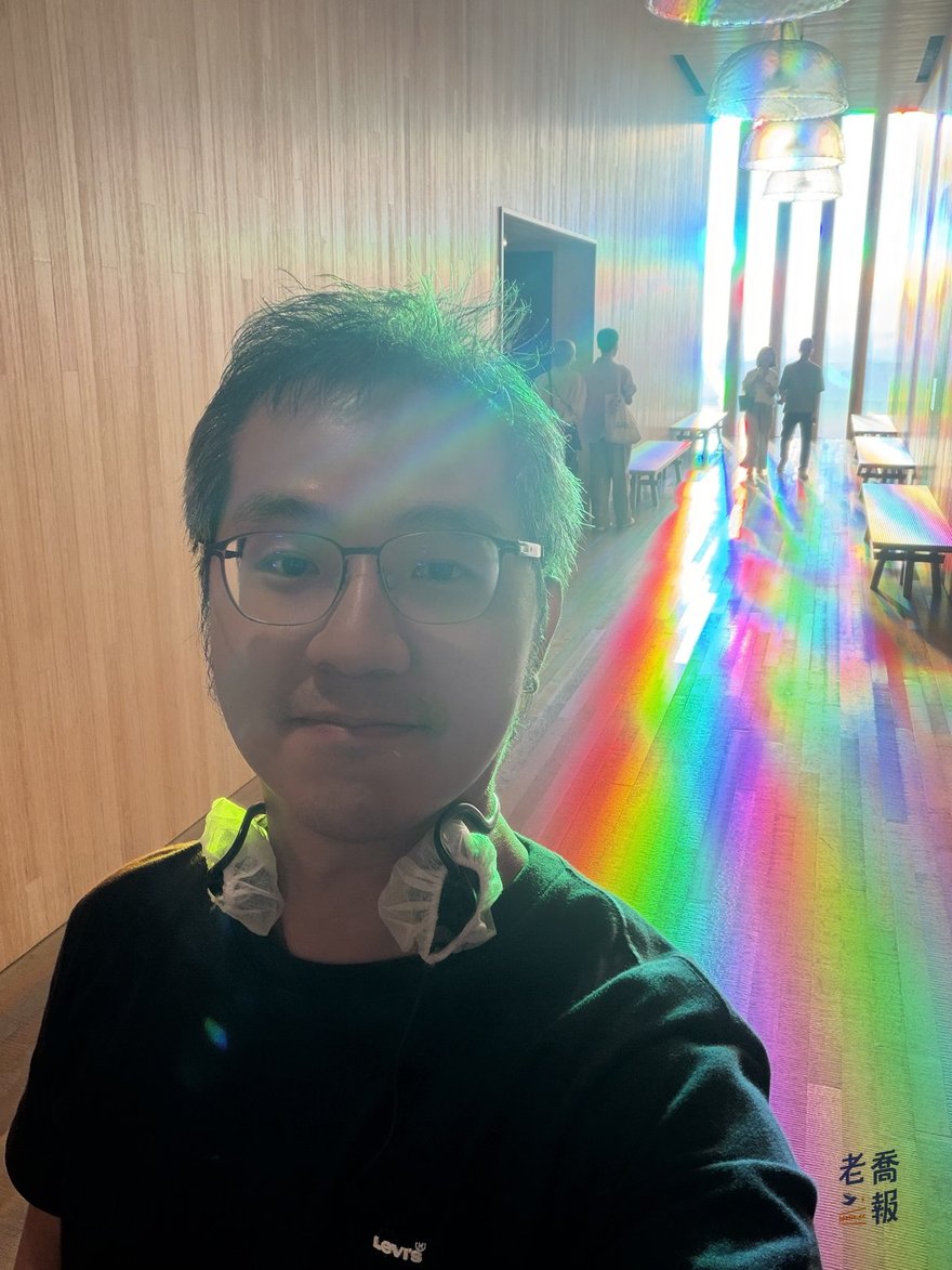 老喬在彩虹長廊自拍，臉上和身後的木牆都映著稜鏡折射出的彩虹光帶