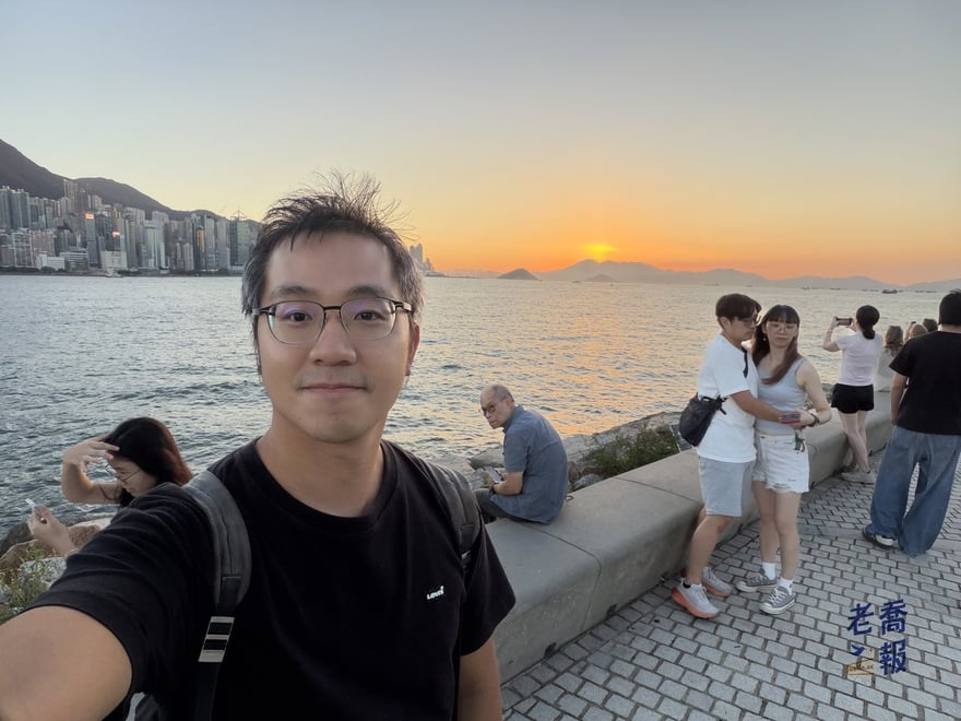 老喬在西九海濱的自拍，背後是正在落下的夕陽和港島西邊的山，海堤上很多人在拍照