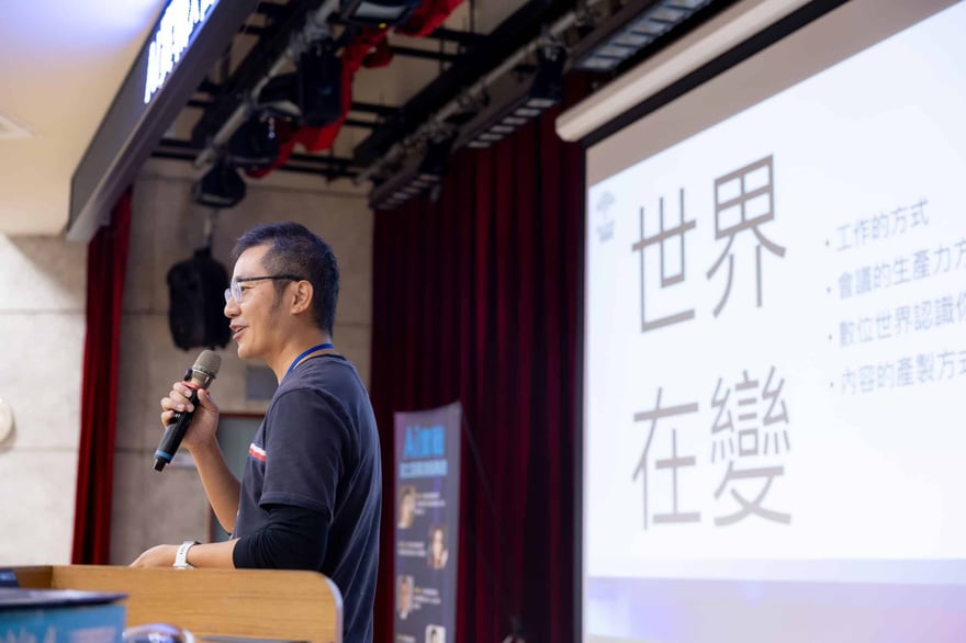 講者在講台旁拿著麥克風說話，右側投影幕上大字寫著「世界在變」，並列出工作的方式與內容的產製方式等項目。