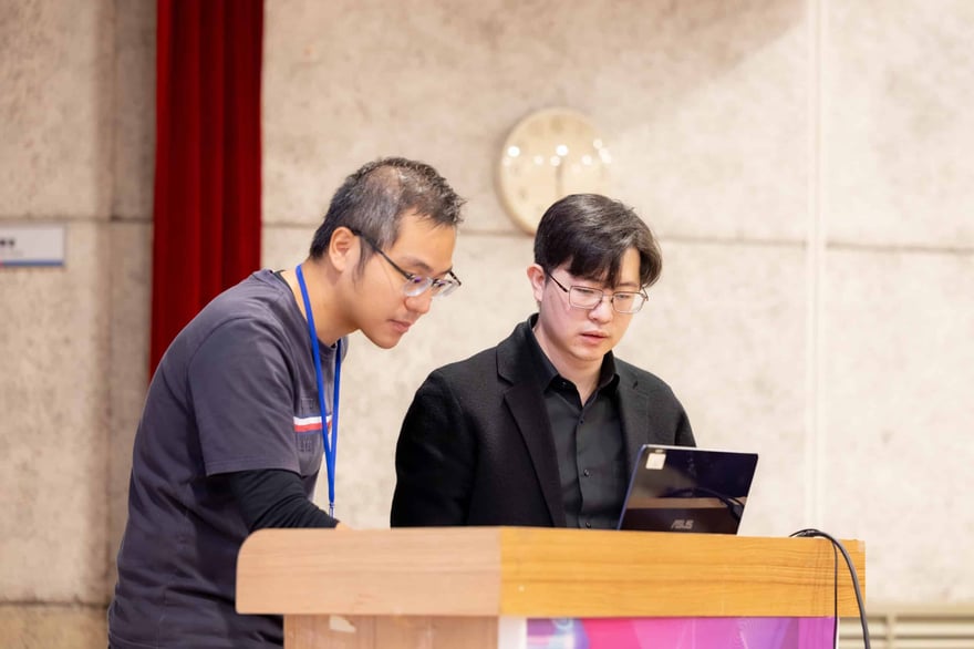 ALT標籤：兩位男士專注於電腦屏幕，進行新聞報導或討論，背景為會議室或演講場地，展現專業新聞工作場景。.