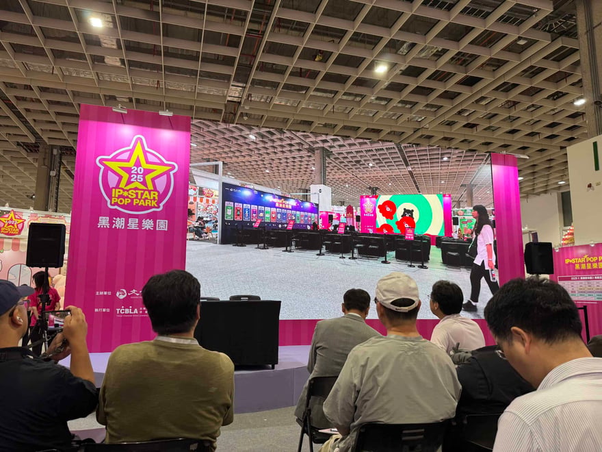Bright pink banners and a large LED screen display at the IP-STAR Pop Park event, showcasing entertainment and technology innovations. Attendees are seated, watching the stage presentation in a spacio.