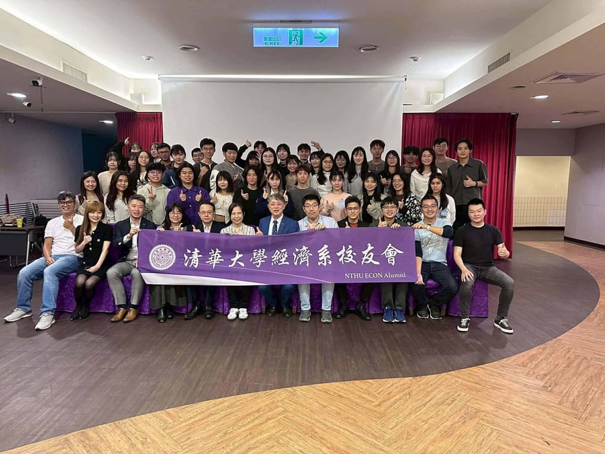 清華大學經濟系校友會活動的大合照，前排坐著講師與校友並舉著紫色橫幅，後排站滿笑著比讚的學生。