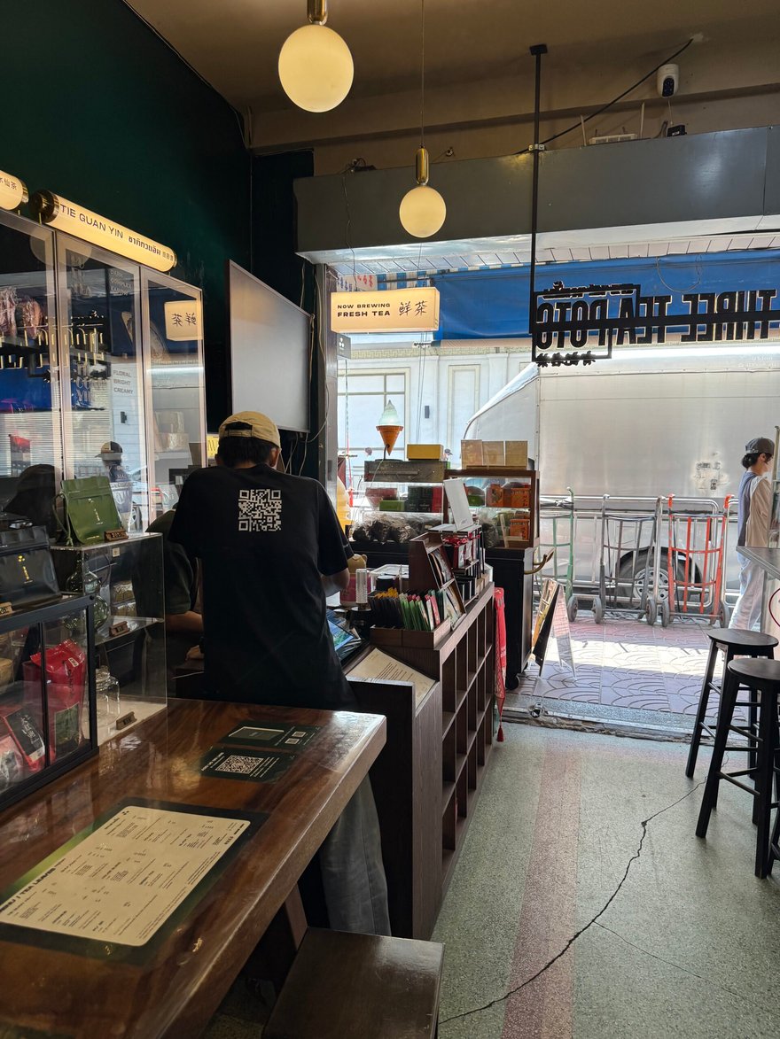 THREE TEA POTS 店內一景，穿黑衣的店員在櫃台後方，兩旁有玻璃櫃與木桌，遠處門外可見街景