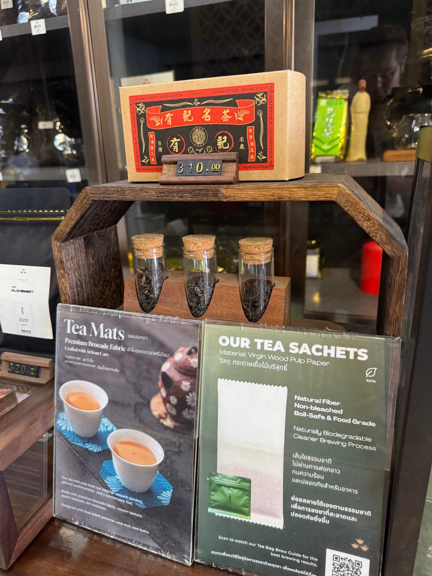店內木架上放著有記名茶紅色茶葉盒與三罐茶葉試管，前方立牌介紹 Tea Mats 與環保茶包 Our Tea Sachets