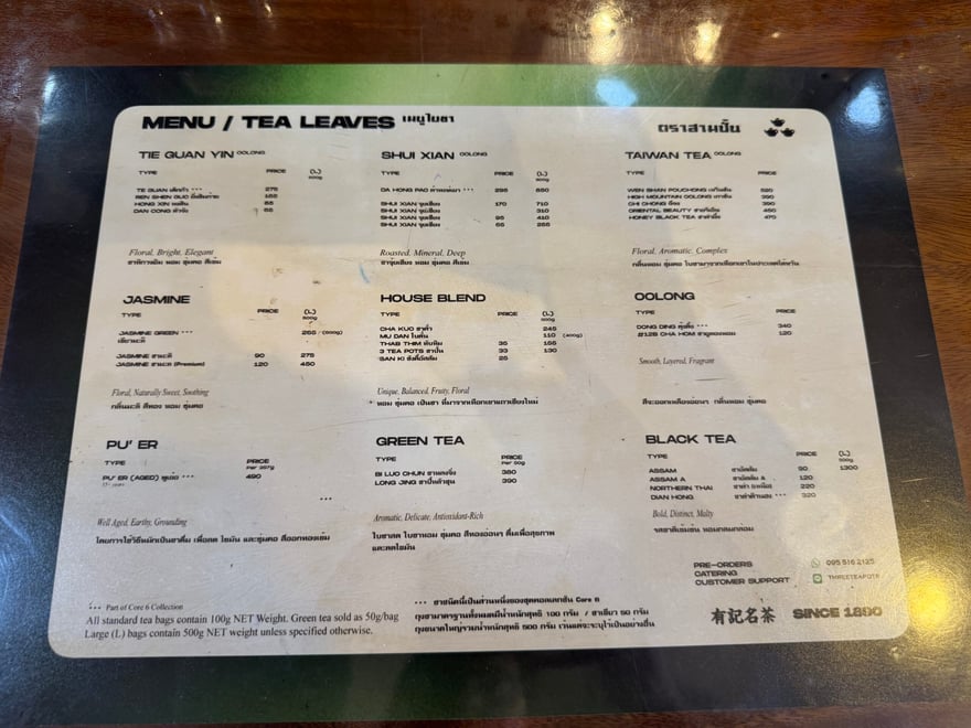 木桌上放著 MENU / TEA LEAVES 茶葉價目表，依鐵觀音、水仙、台灣茶、茉莉、黑茶等分類列出品項與價格