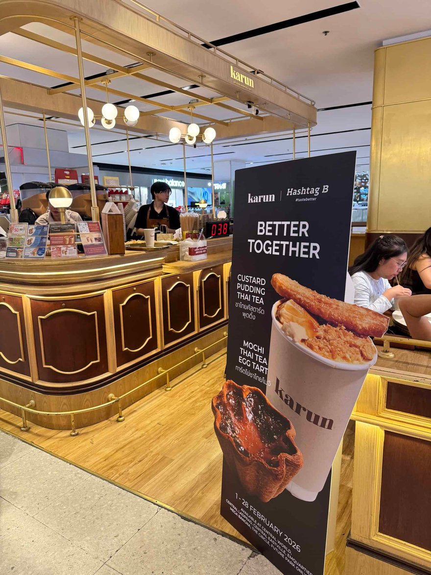 Karun 泰奶店面，木質櫃台上方掛著燈飾，門口立著寫有 BETTER TOGETHER 的看板與泰奶杯圖