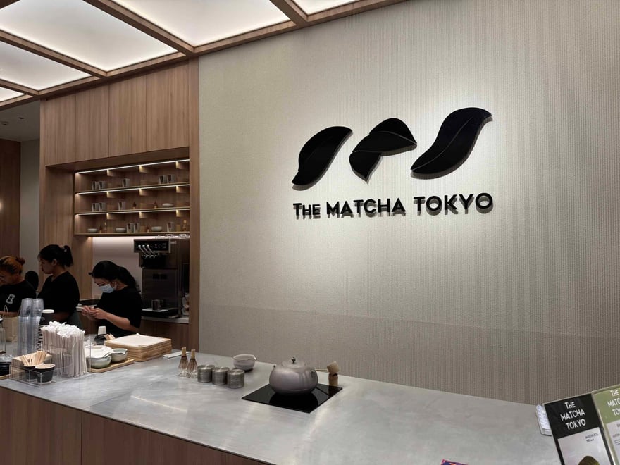 The Matcha Tokyo 店內，牆上有黑色葉片造型店名標誌，下方吧台有店員與茶具
