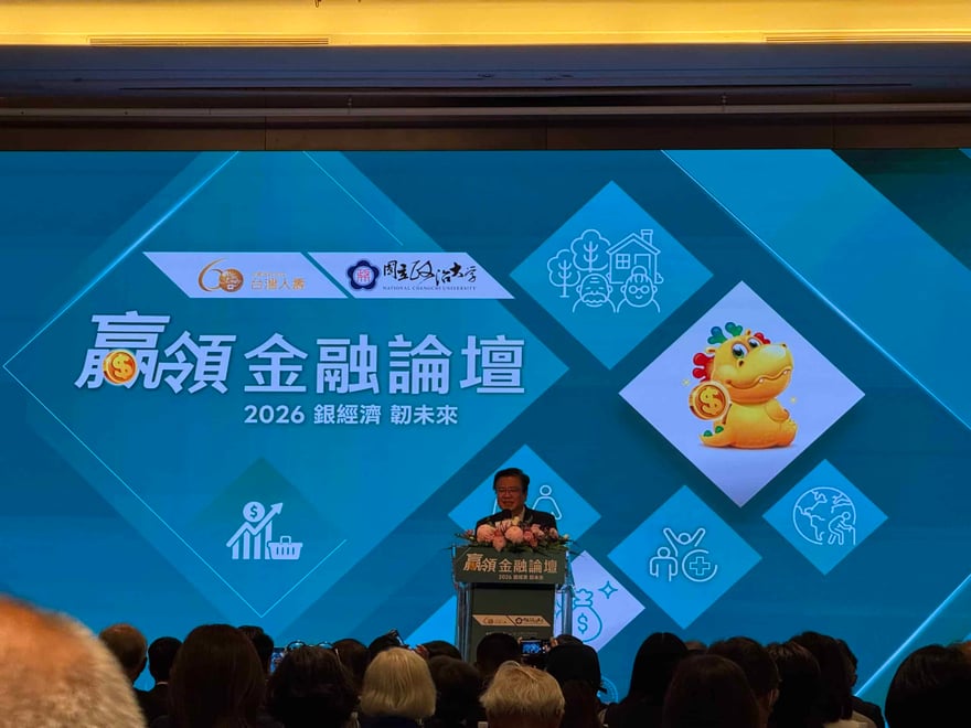 2026 贏領金融論壇舞台，背景螢幕寫著「贏領金融論壇 2026 銀經濟 韌未來」，主辦方為台灣人壽與國立政治大學，講者站在花飾講台後